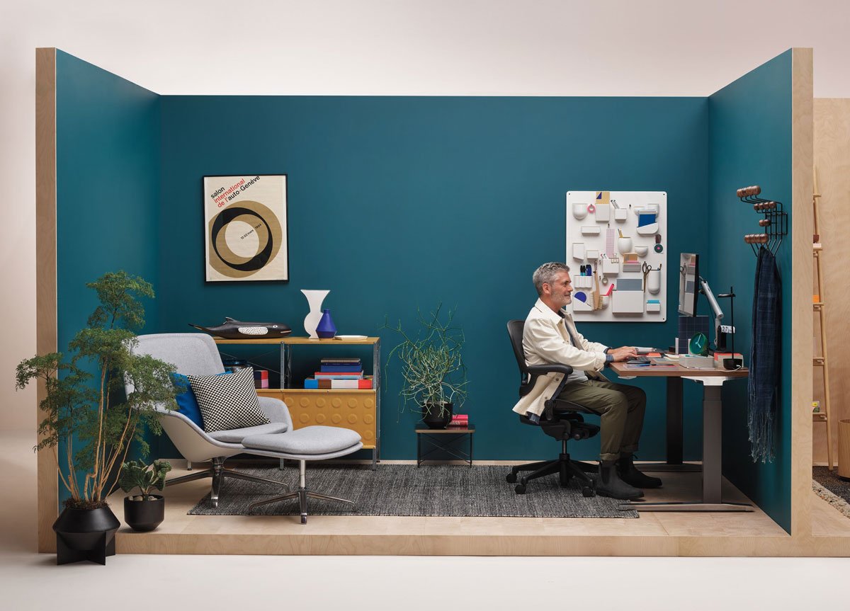 Man sat in corner home office setting that includes Aeron home office chair in graphite infront of Jarvis sit stand desk with black legs and wood top