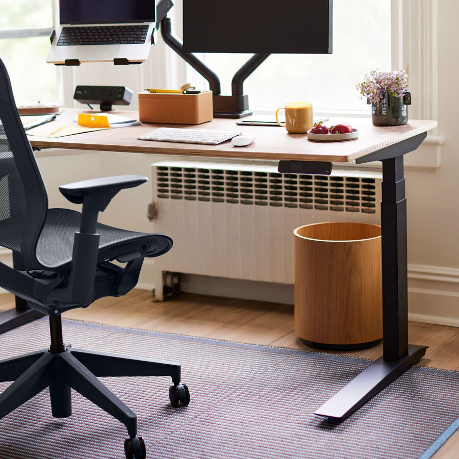 Home office setting with partial view of high back Cosm office chair in nightfall in front of Jarvis sit-stand desk with black legs and wooden top