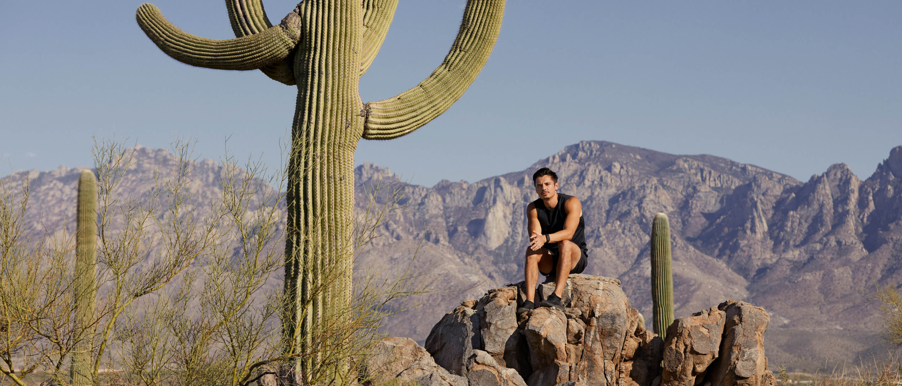 Gamer Xaryu sat on rocks in rocky mountainous outdoor space with large cacti surrounding him